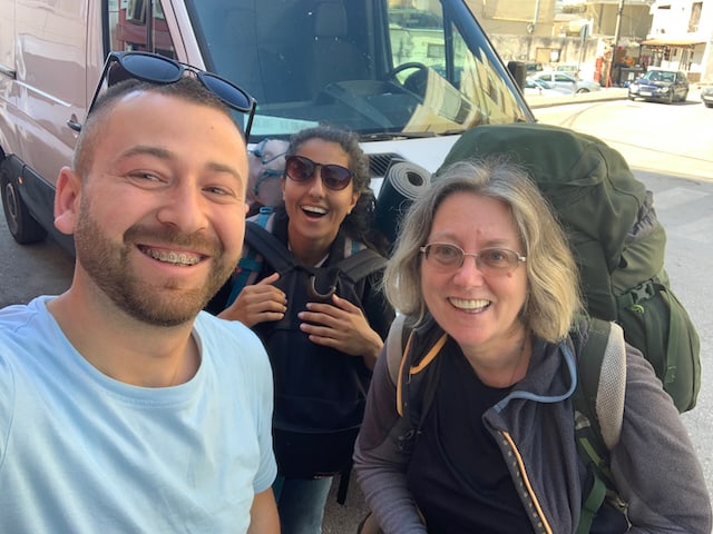 A man wearing a blue top taking a selfie with two women hitchhikers