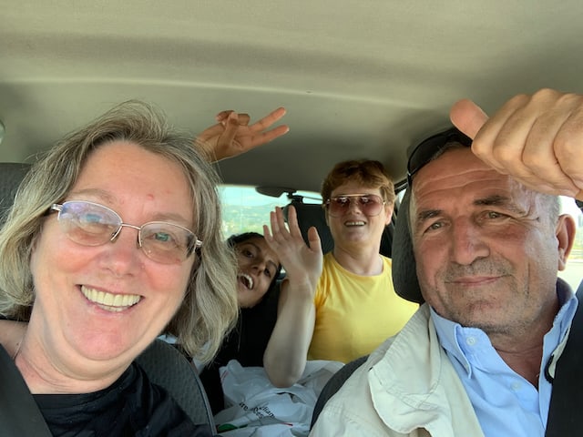 A man wearing a blue shirt taking a selfie with three women inside a car
