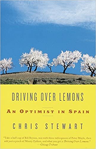 Book Cover of 'Driving Over Lemons' - blossom trees on a hill with blue sky