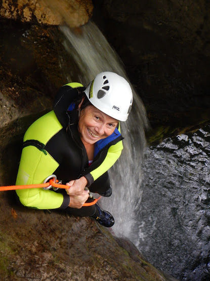 Woman canyoning with a white safety helmet, yellow jacket, an orange climbing rope and other safety equipment