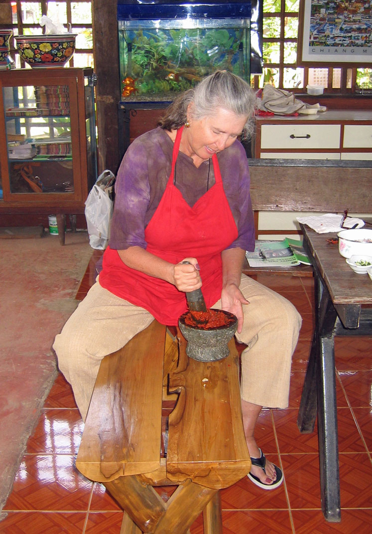 Red curry paste is pounded with a wooden pestle in a wooden mortar