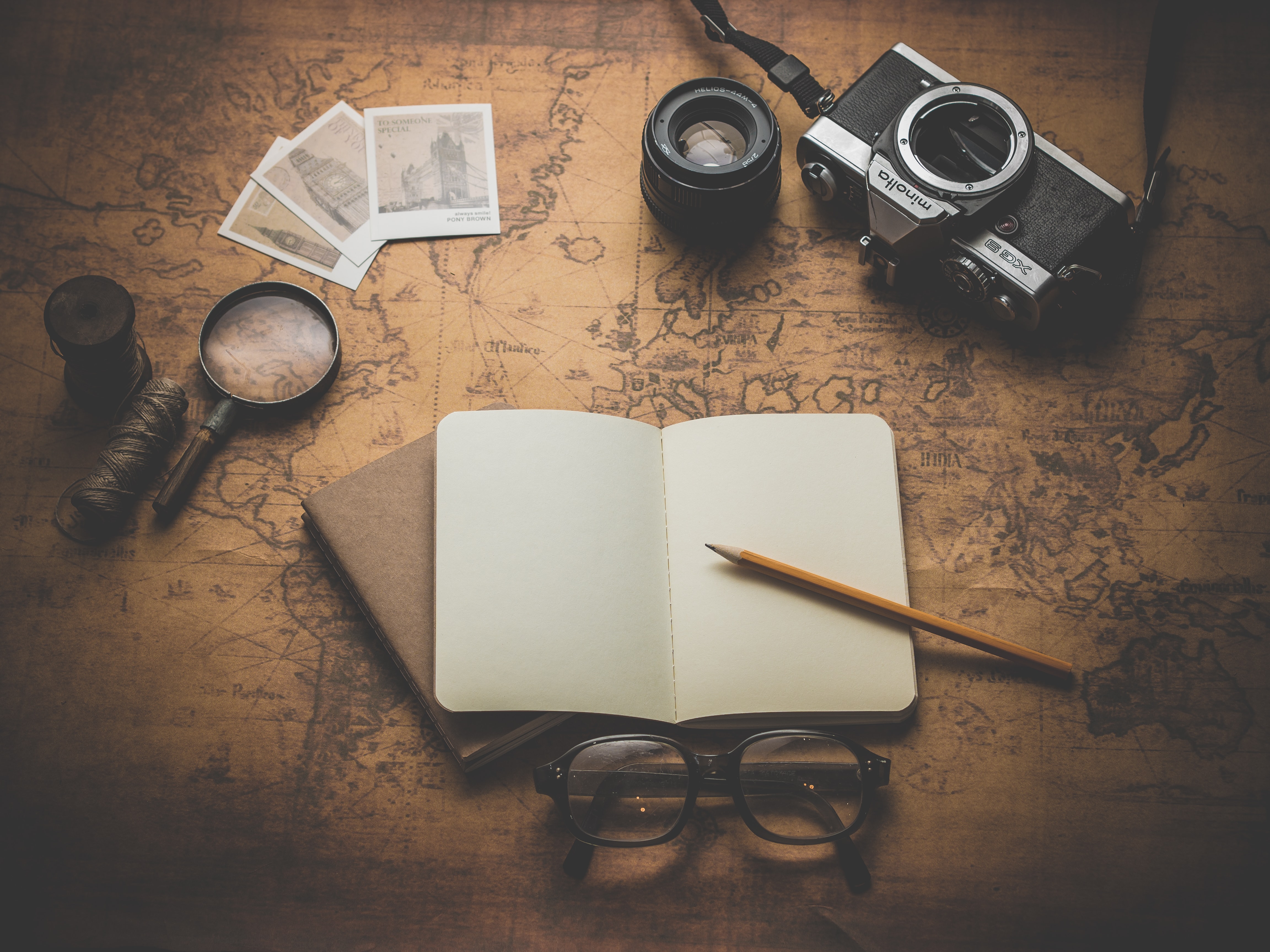 A notebook and pencil with spectacles, a camera and a map