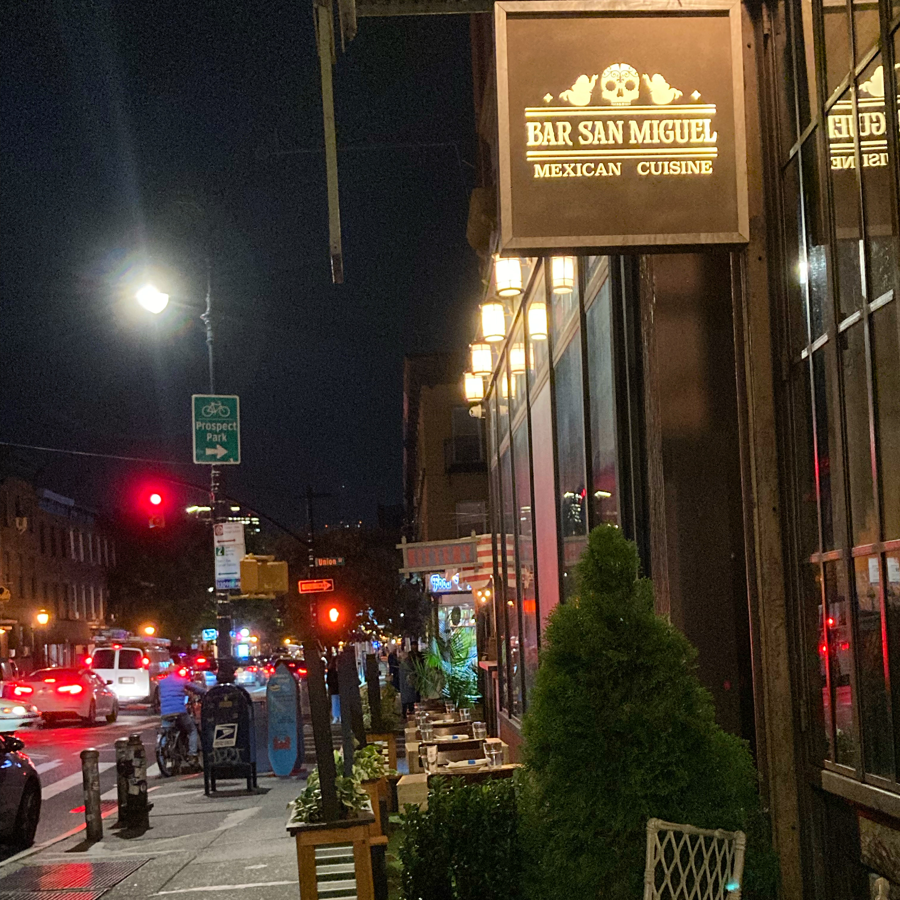 A street scene at night in Brooklyn with a "Bar San Miguel" sign