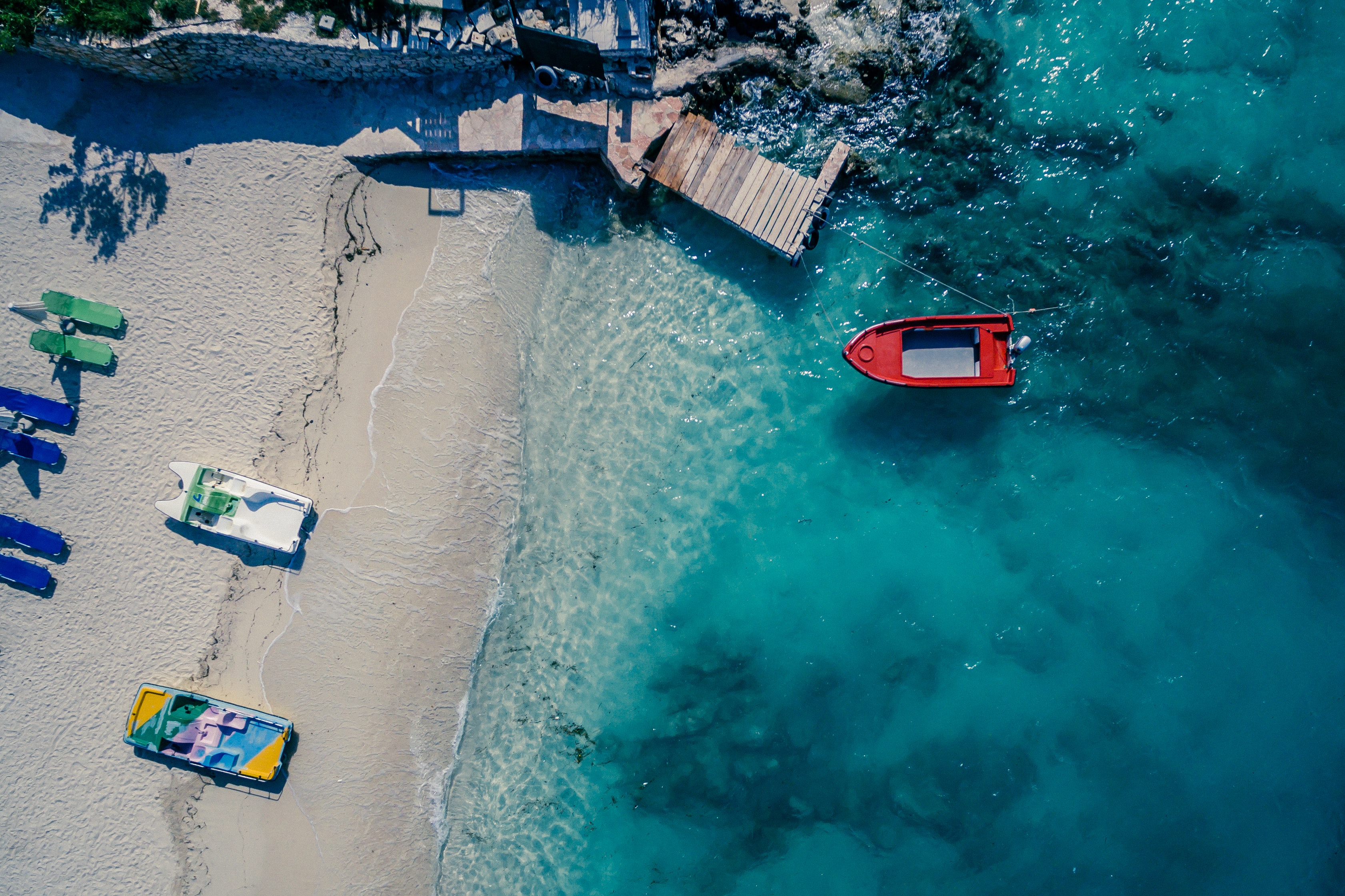 Looking down on a beach with blue water and a red boat
