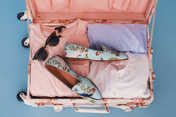 Lady's travel case packed with pink clothes and flowery shoes