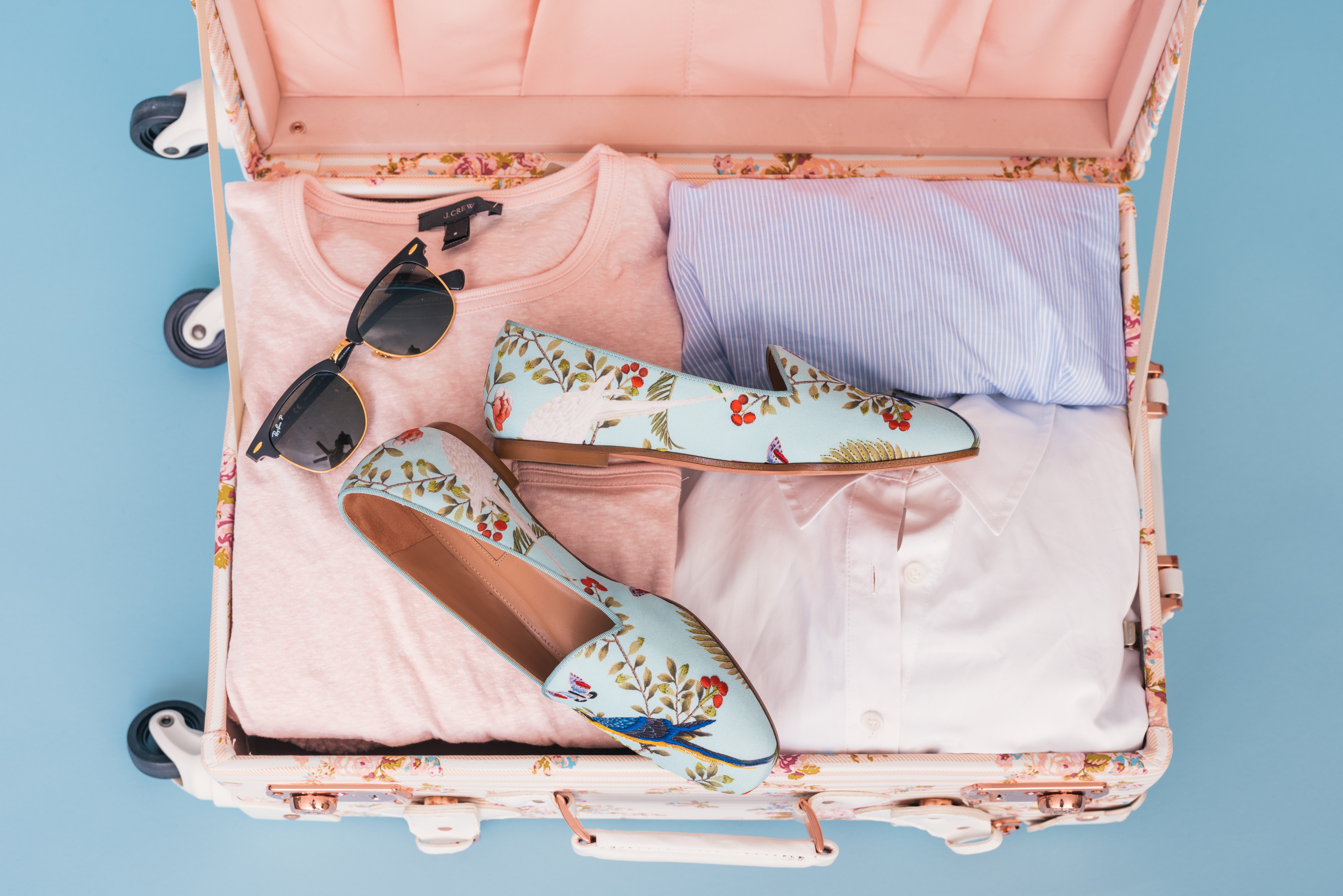A woman's suitcase containing some pink clothes, a pair of shoes, and sunglasses.