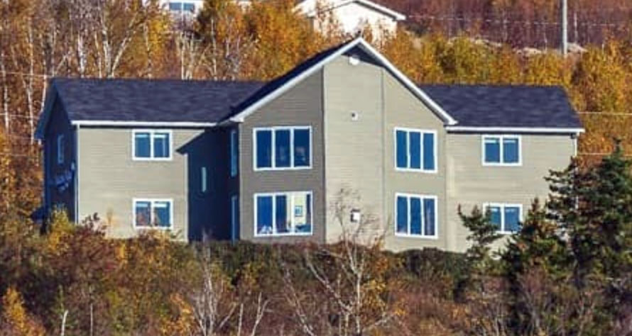 A 2 storey grey house on a hillside surrounded by trees