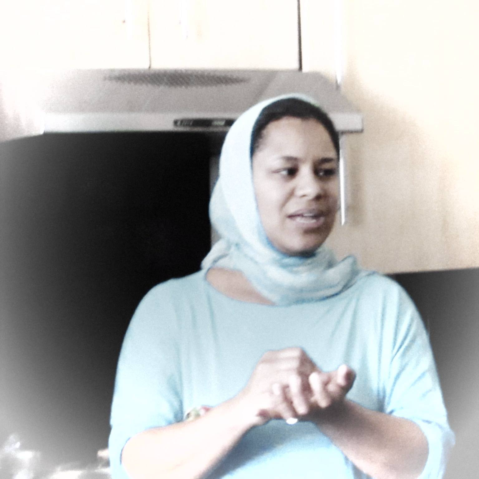 A woman wearing a light blue top and head covering delivering a speech