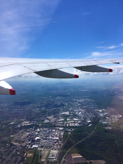 An aircraft wing against blue sky, viewed from inside the plane, with a city below.
