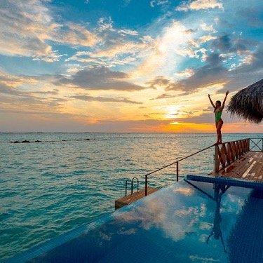 A woman standing on a pool deck by the sea at sunset.