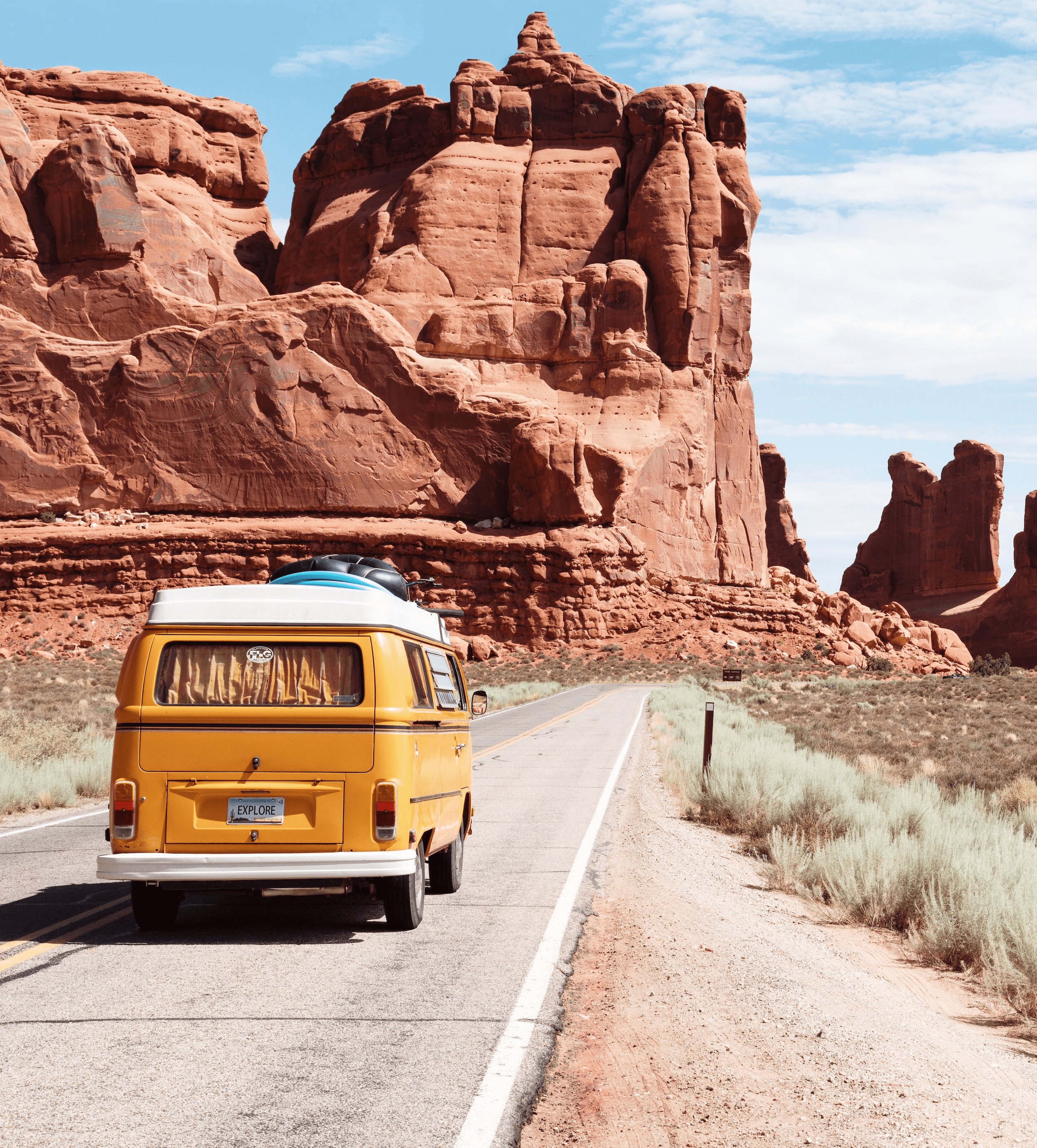 A yellow VW camper van in the desert with rock outcrops in the background.