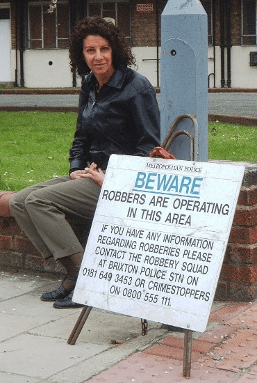 Bambi Vincent sitting beside a Police sign warning of pickpockets