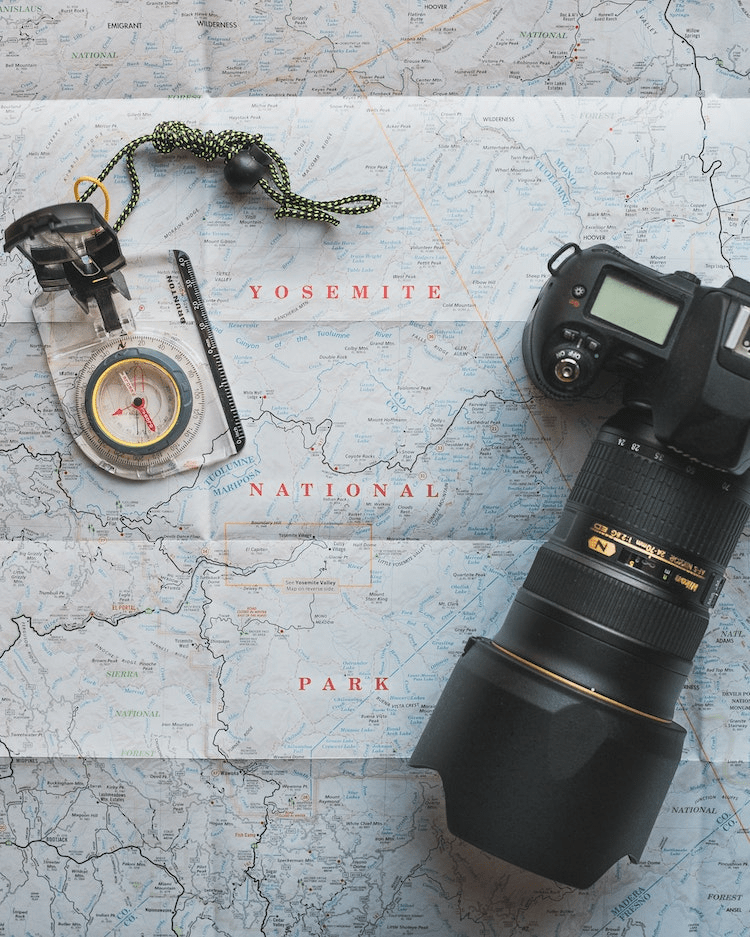 A camera with a telephoto lens, a compass and a map of Yosemite National Park.