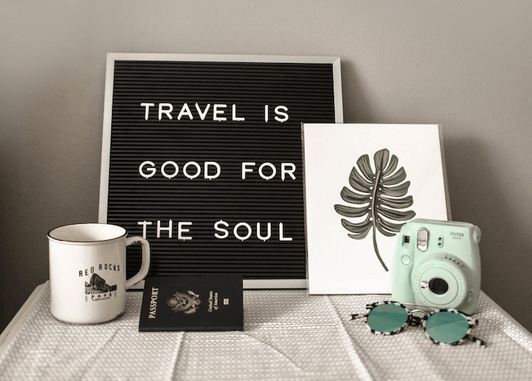 Travel related items in a small table, including a passport, a camera, sunglasses and a mug