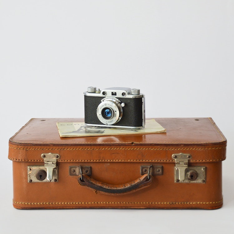 An old brown leather suitcase with a camera sitting on it.