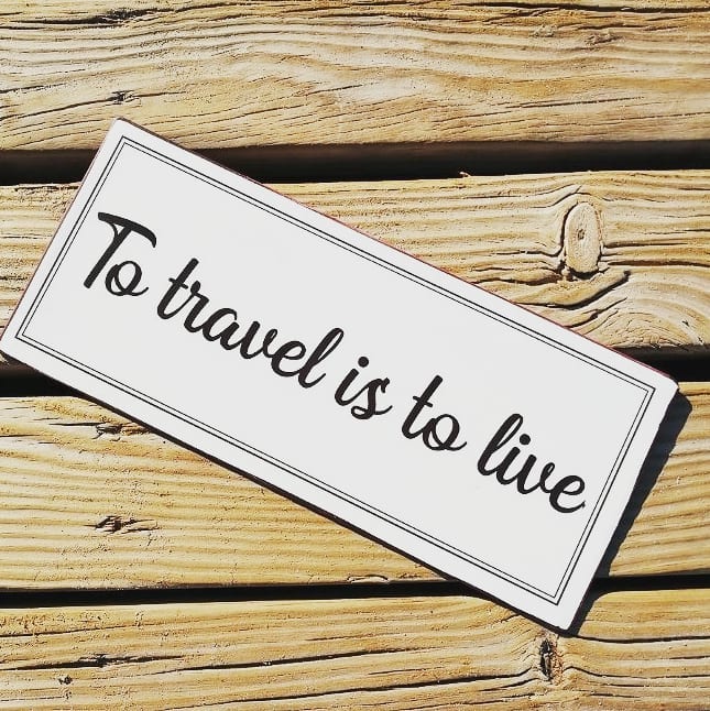 to travel is to live quote - plaque on wood background