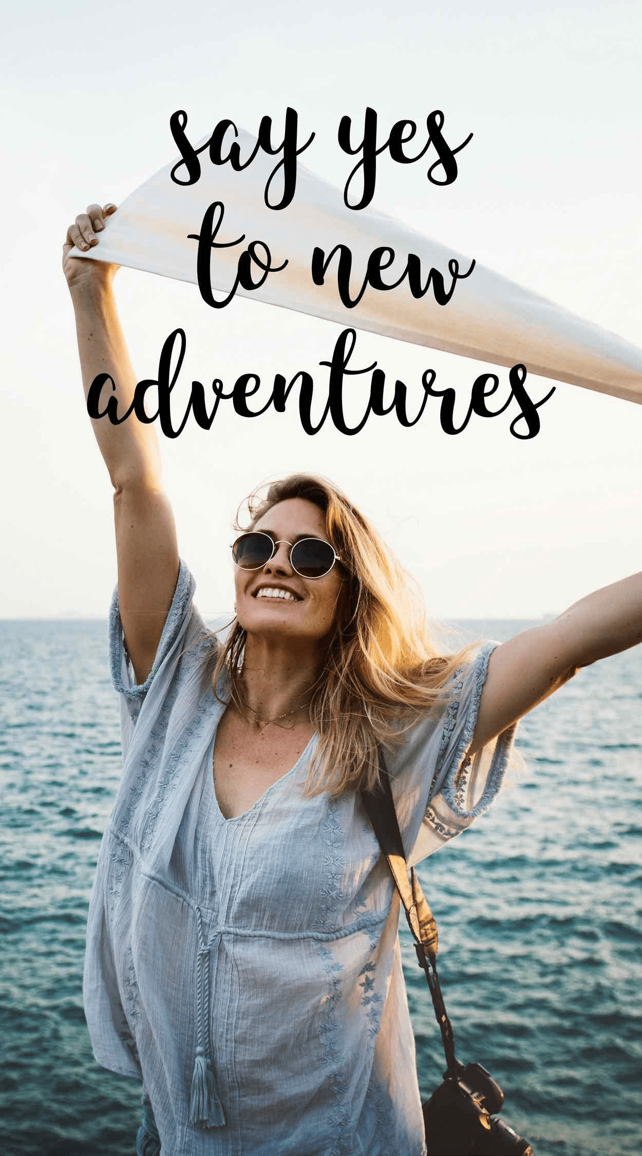 A woman wearing sunglasses in front of the sea, raising her arms to a new adventure.